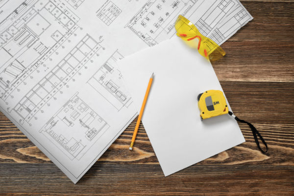 Blueprints, pencil, protective glasses, steel tape, pencil and white paper lying on wooden table background.