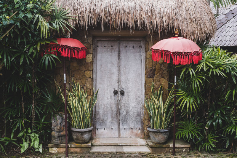 Entrance in traditional bali house with wooden door, straw roof and red umbrellas